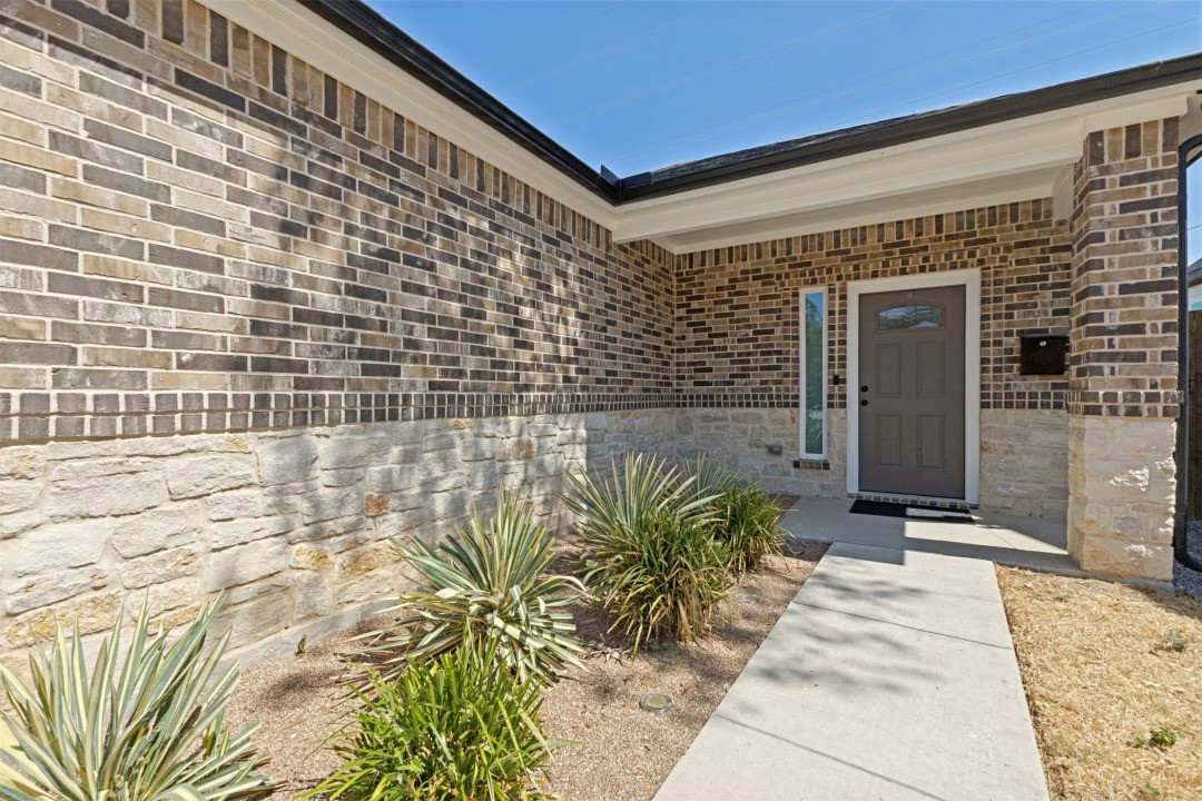 Home entrance with a recessed gray door, brick and stone facade, and yucca landscaping along the walkway.