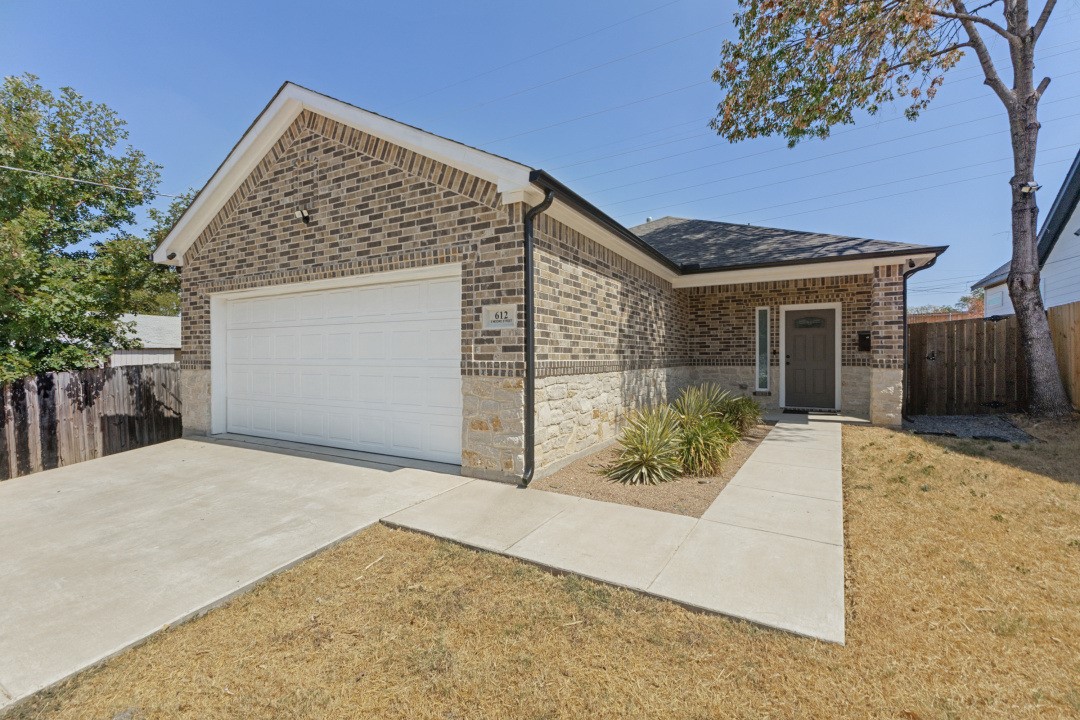Brick house with a white double garage door, stone base, and concrete walkway to the entrance.