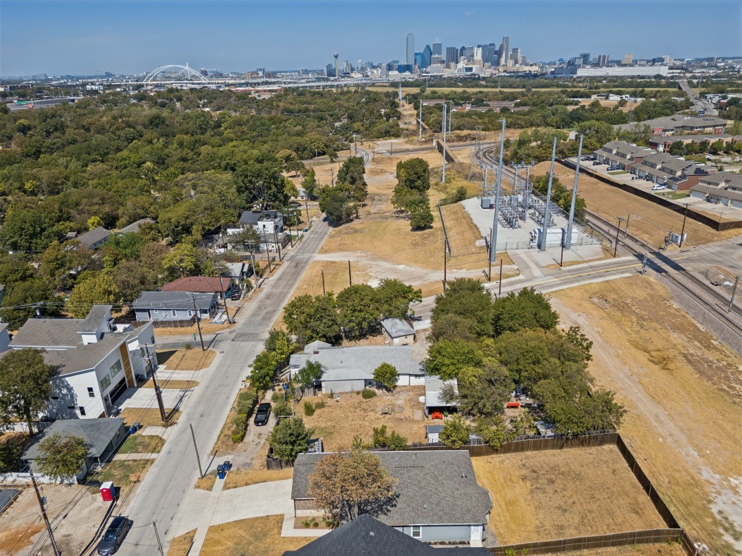 Aerial view of neighborhood with open lots, rail lines, and downtown Dallas skyline.