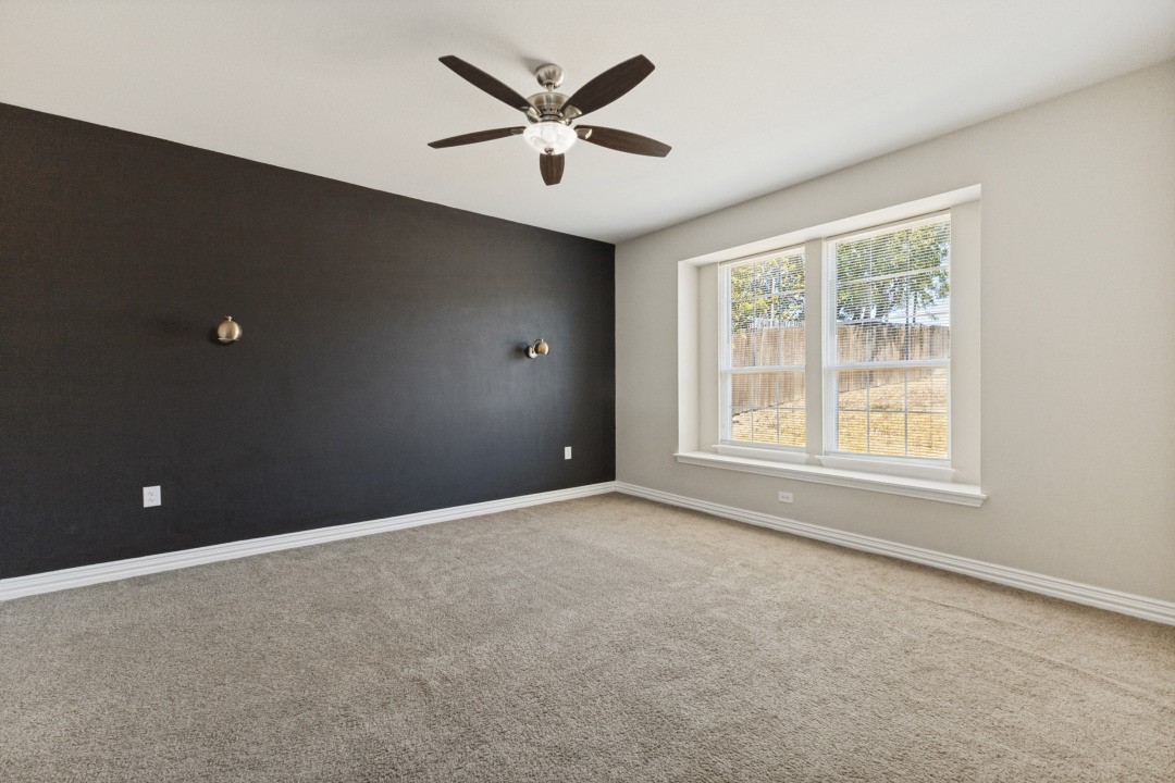 Empty bedroom with a dark accent wall, ceiling fan, and large double window.