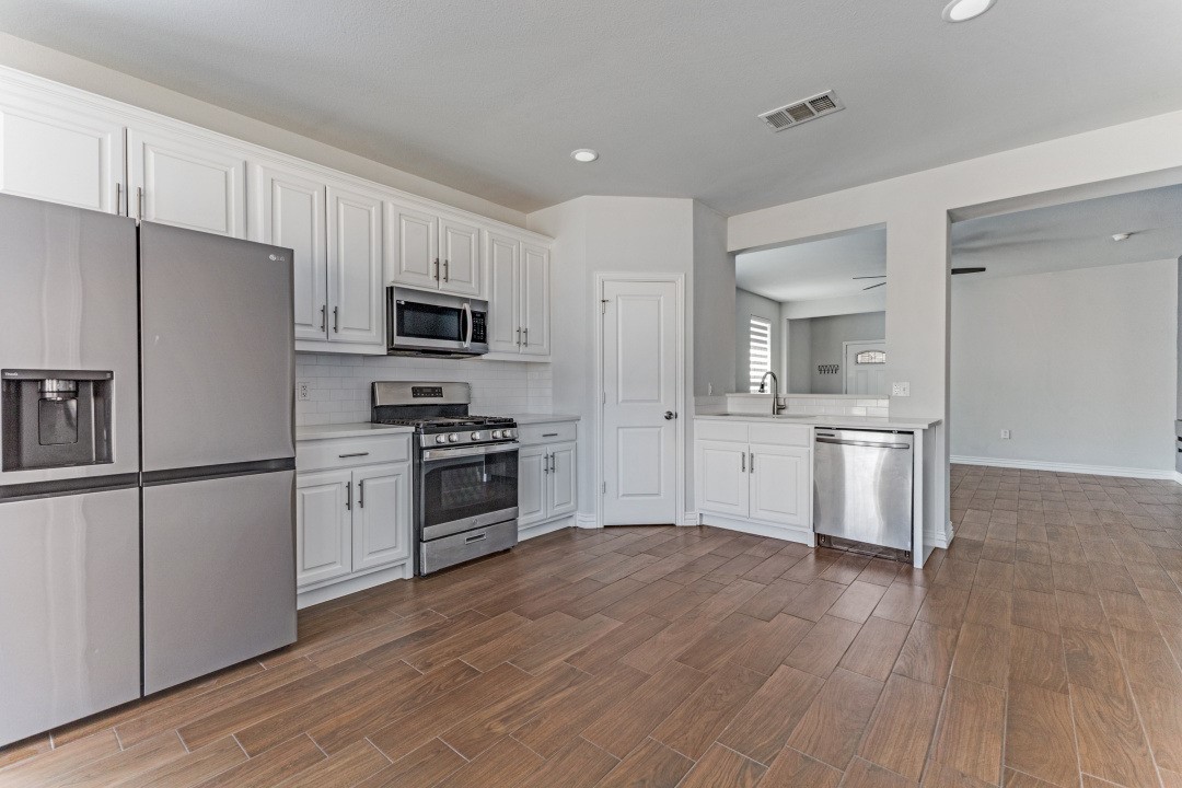 Unfurnished kitchen with white cabinets, stainless steel appliances, and brown tile flooring.