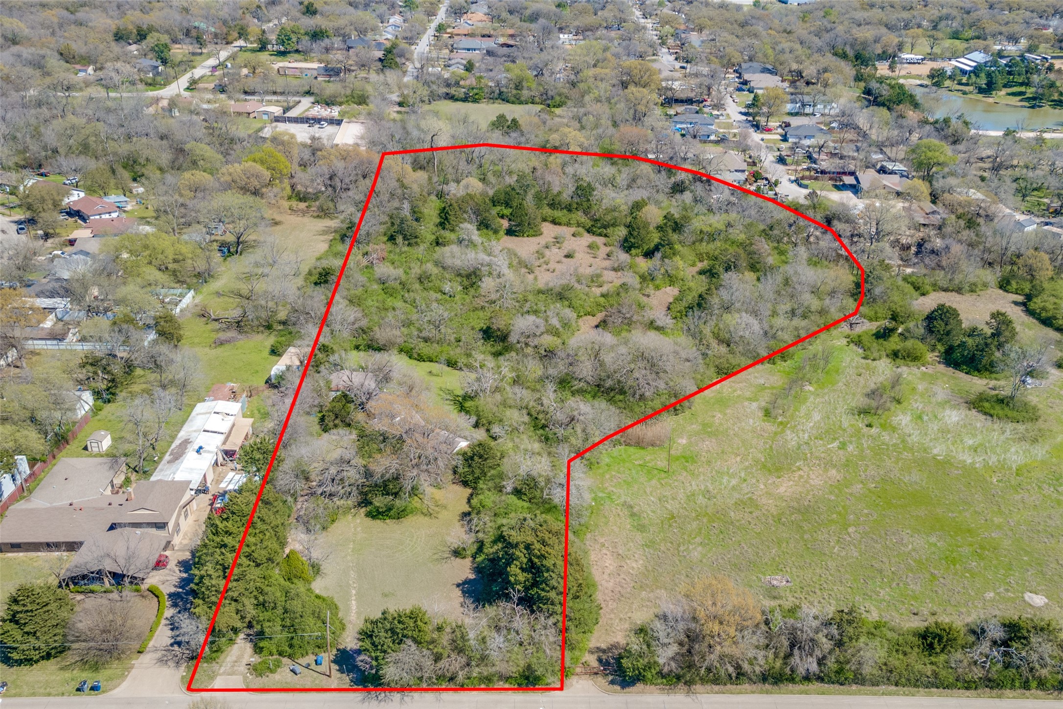 Aerial view of a wooded property outlined in red, with open clearings and neighboring homes.