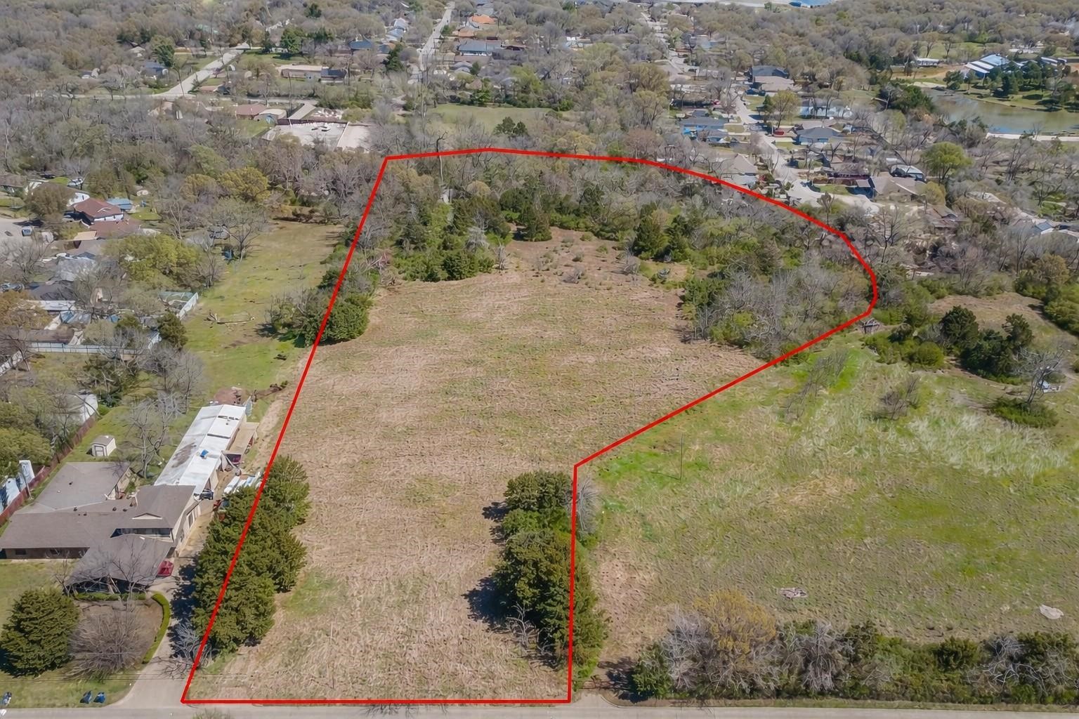 Aerial view of a cleared residential lot outlined in red, bordered by trees and neighboring homes.
