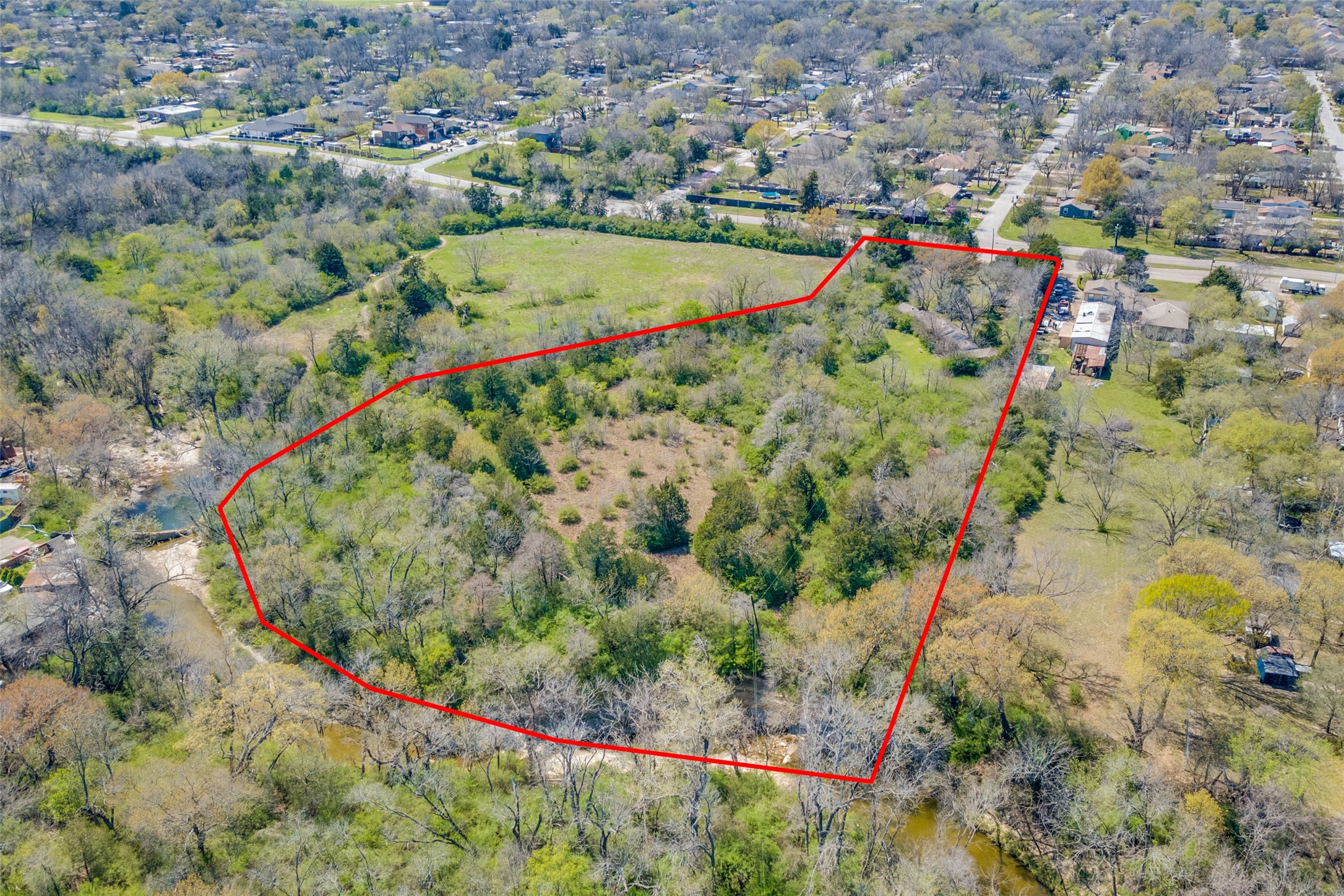 Aerial view of a wooded property outlined in red, with a central clearing and creek along the edge.