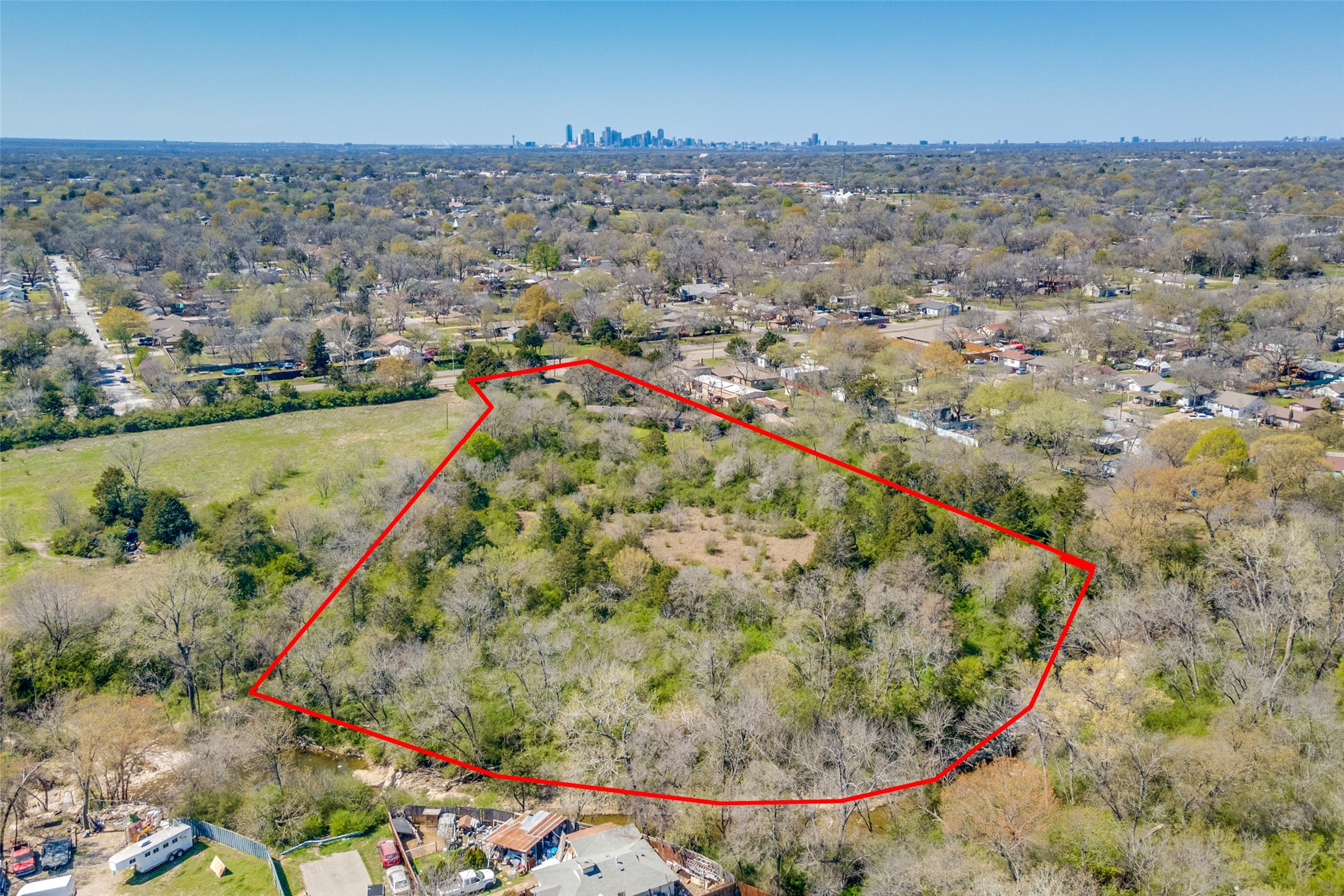 Wooded property outlined in red, with a clearing and distant Dallas skyline.