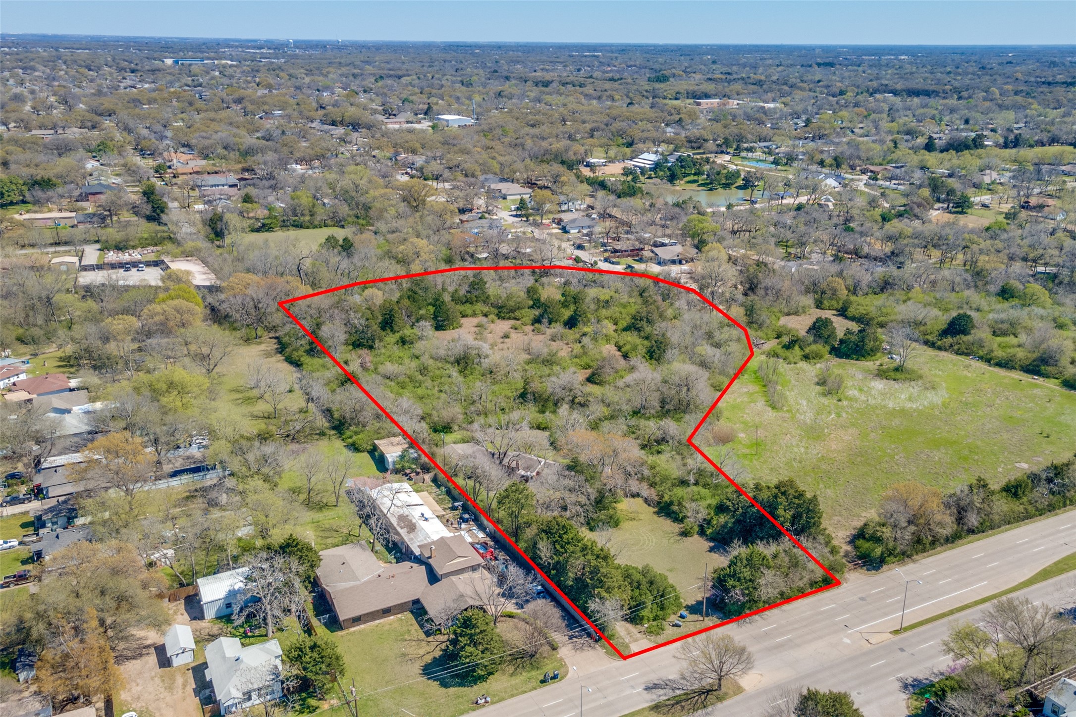 Aerial view of a wooded property parcel outlined in red beside a road.