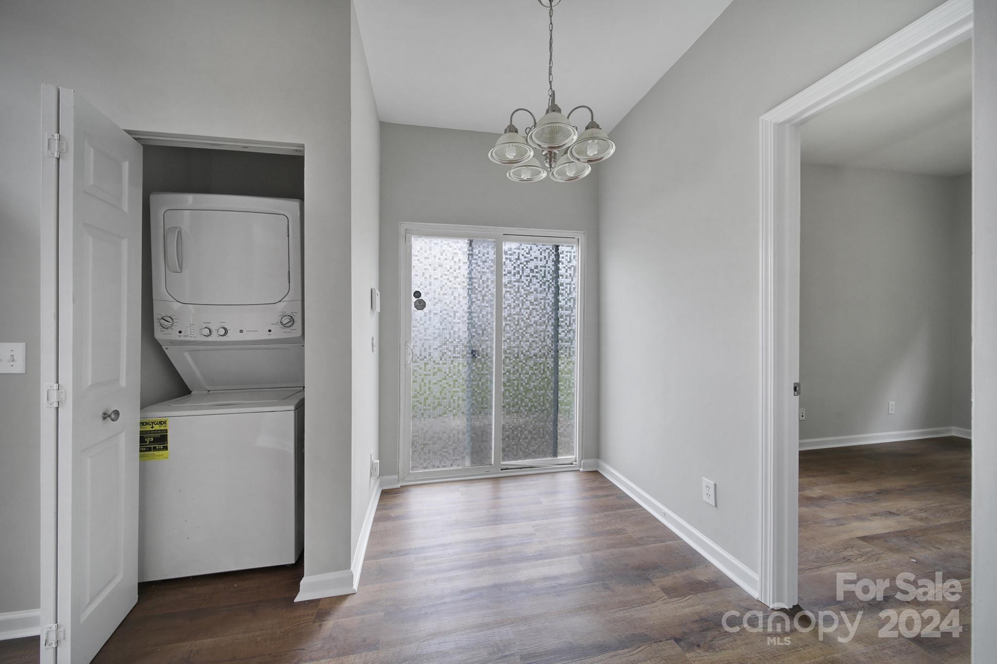 Laundry area with stacked washer and dryer, sliding glass door, and wood-look flooring.