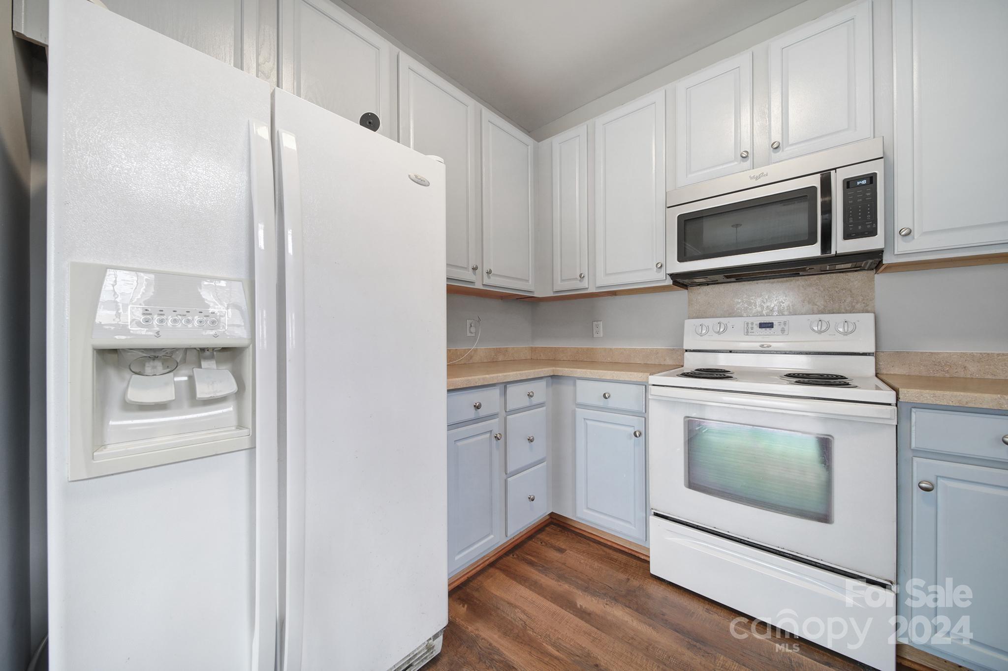 Kitchen with white appliances, pale blue lower cabinets, beige countertops, and wood-look flooring.