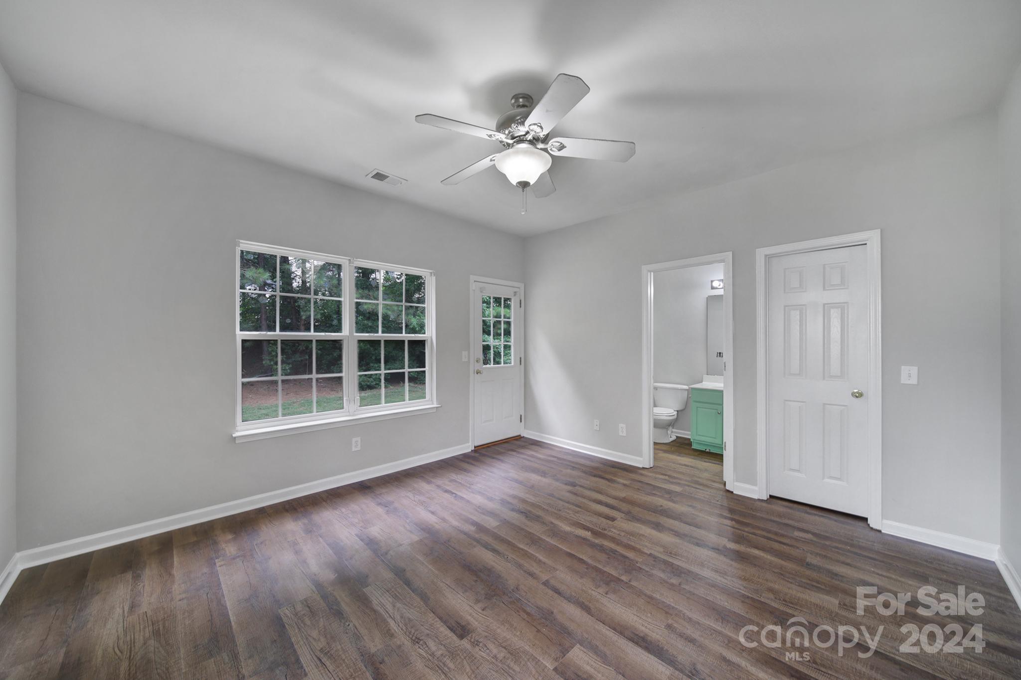 Vacant bedroom with dark wood-look floors, a ceiling fan, and windows overlooking trees.