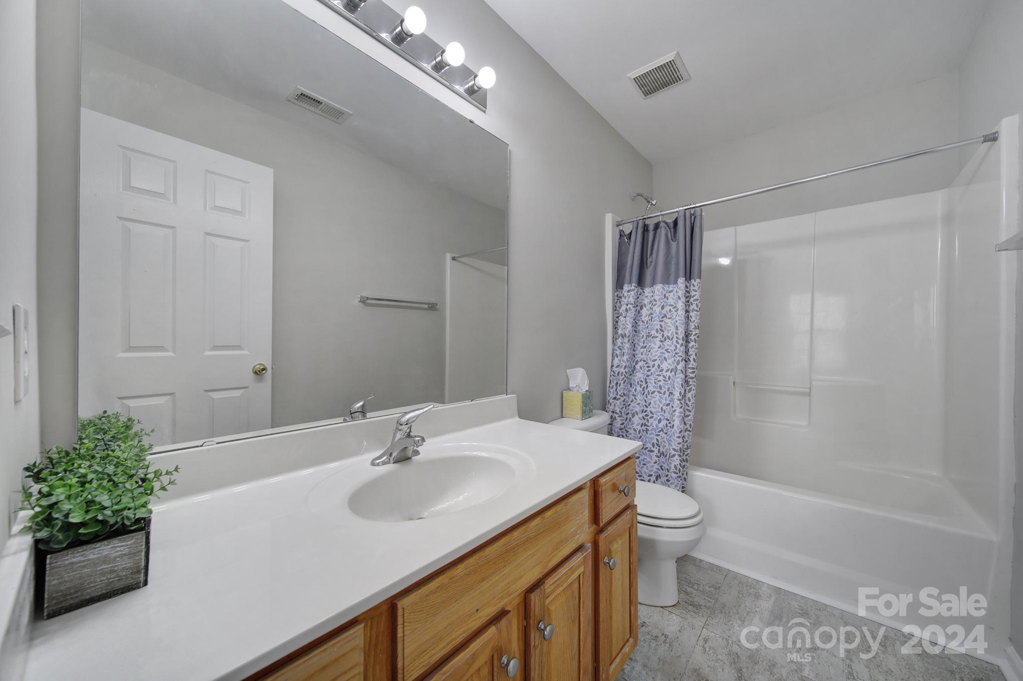 Bathroom with a wood vanity, large mirror, and tub behind a patterned shower curtain.