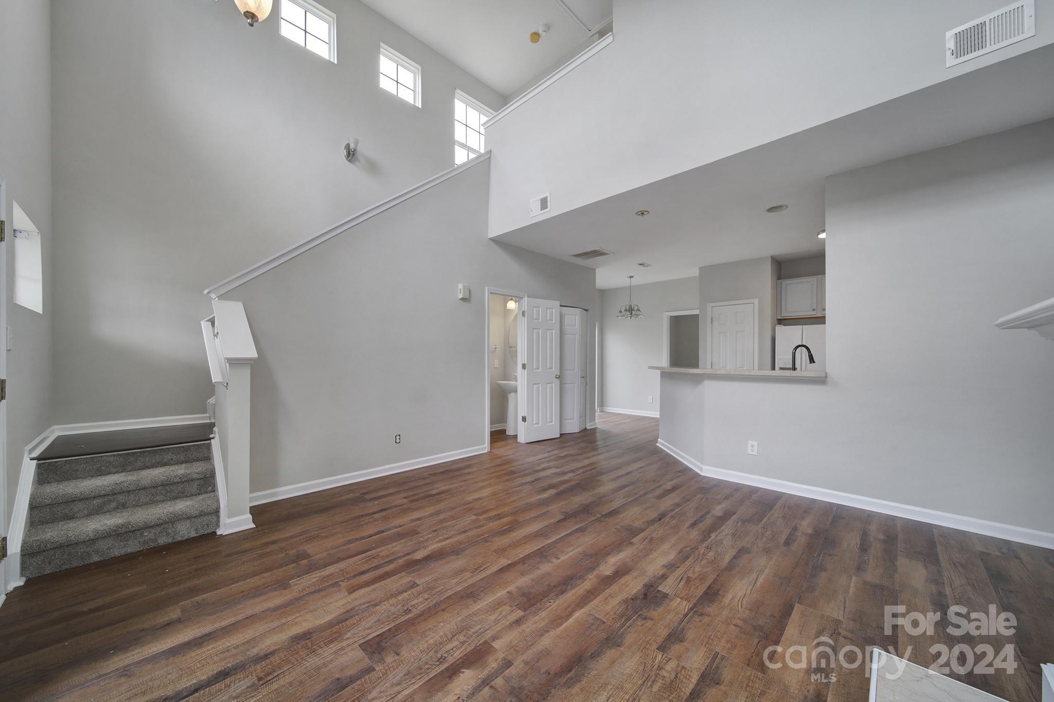 Vacant living area with vaulted ceilings, a carpeted staircase, wood-look floors, and a kitchen pass-through.