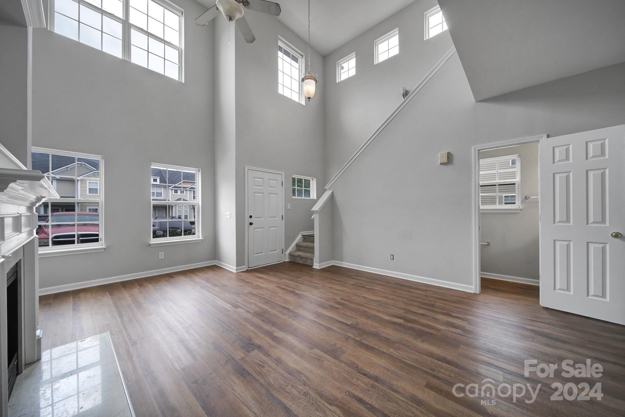 Two-story living room with tall windows, dark wood floors, staircase, and white fireplace.