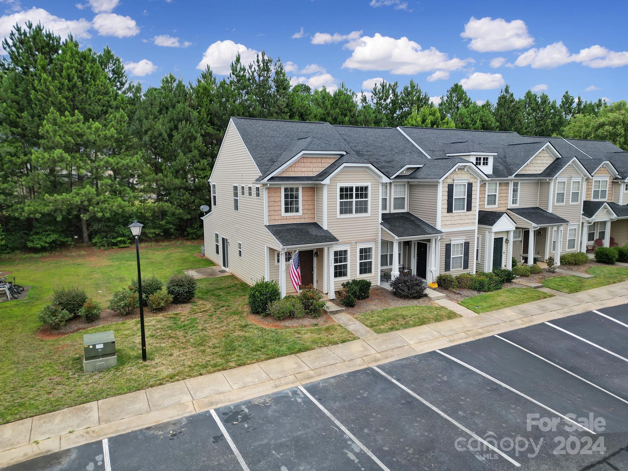 Townhouse exterior with attached neighboring homes, front porches, landscaped lawn, and parking spaces.