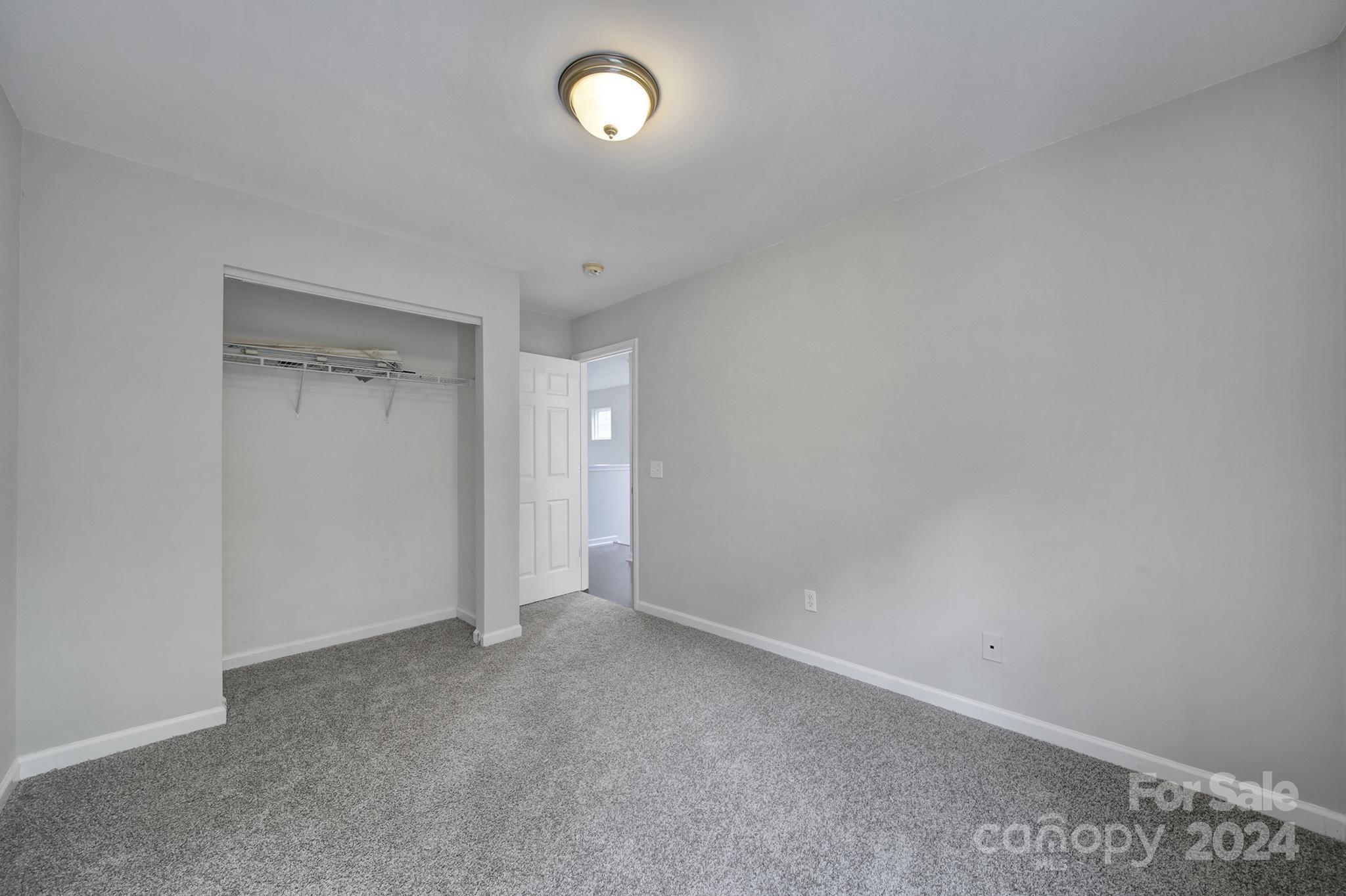 Empty bedroom with gray carpet and an open closet with a wire shelf.