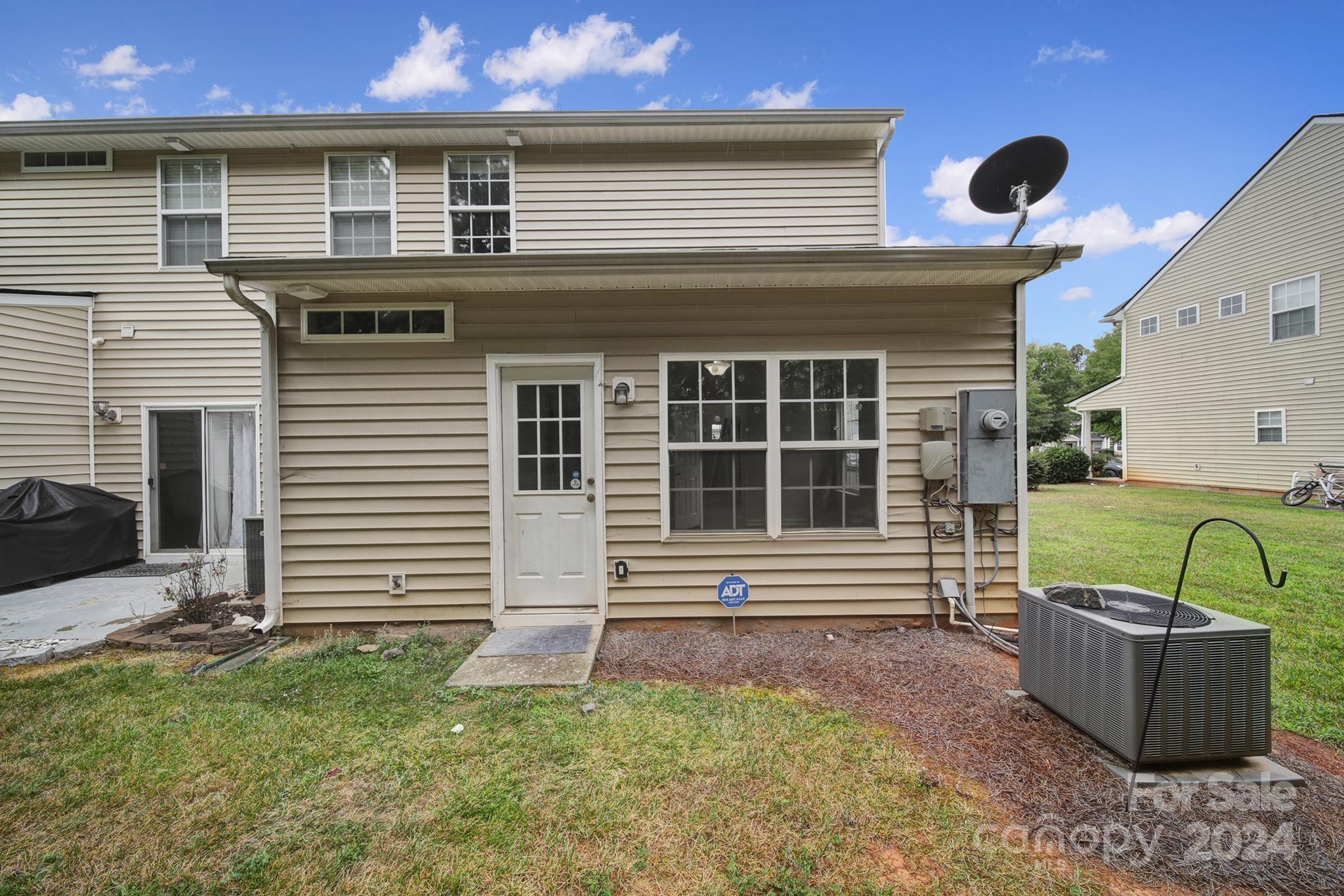 Rear of a beige two-story home with a covered back entrance, large windows, and an outdoor air-conditioning unit.