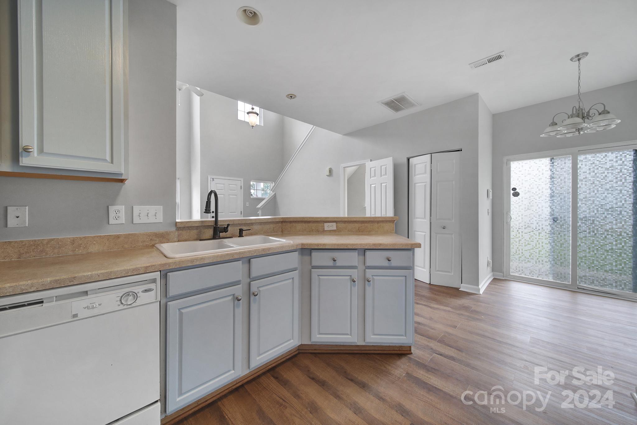 Kitchen with gray cabinets, tan counters, a double sink, and sliding glass doors opening to a wood-floored living area.