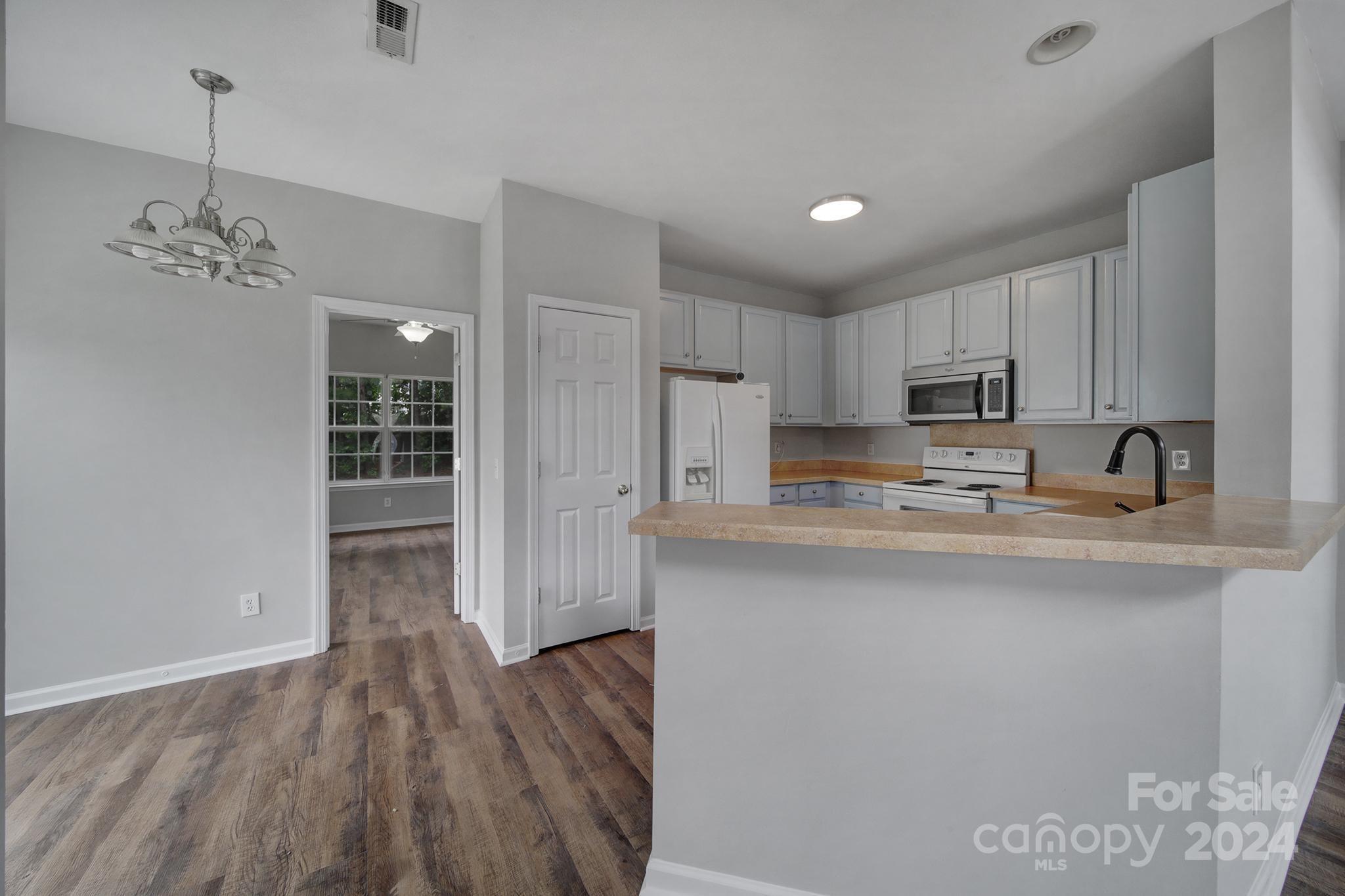 Vacant kitchen with white cabinets, tan counters, a raised breakfast bar, and wood-look flooring.