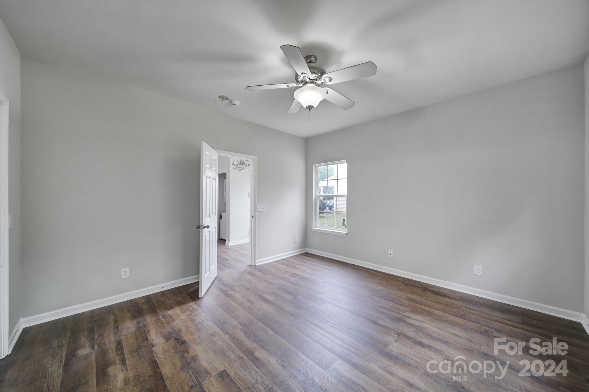 Empty bedroom with dark wood-look floors, a ceiling fan, and a window.