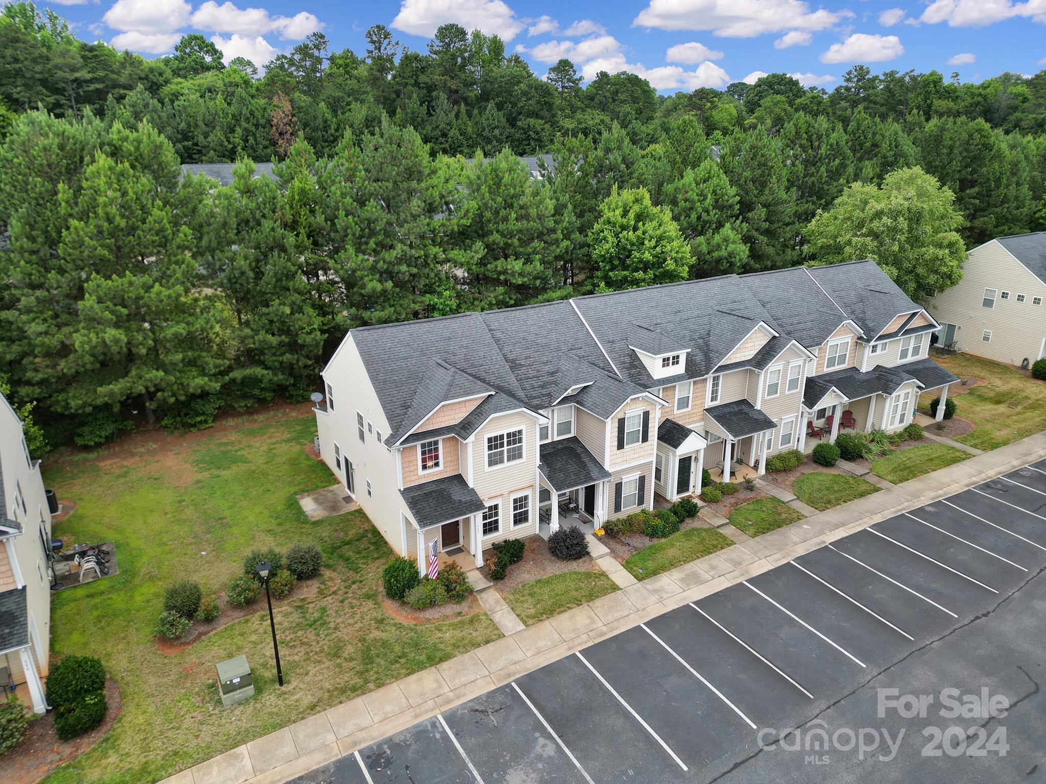 Aerial view of attached townhomes beside a large parking lot and wooded area.