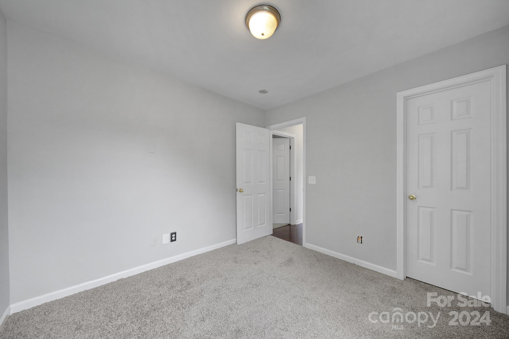 Empty carpeted room with gray walls, two white paneled doors, and a ceiling light.