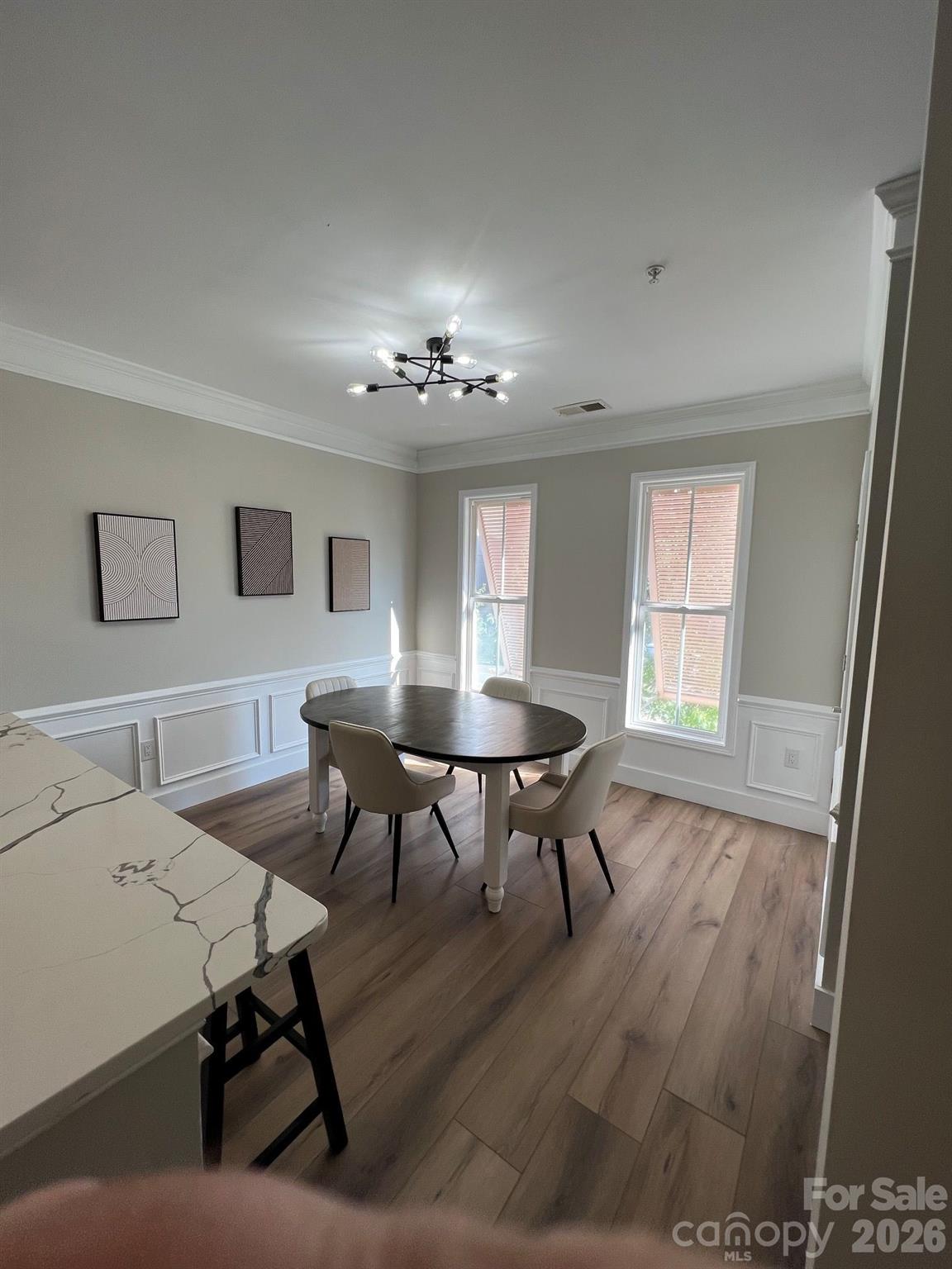 Dining room with oval table, paneled walls, tall windows, and a marble-look island.