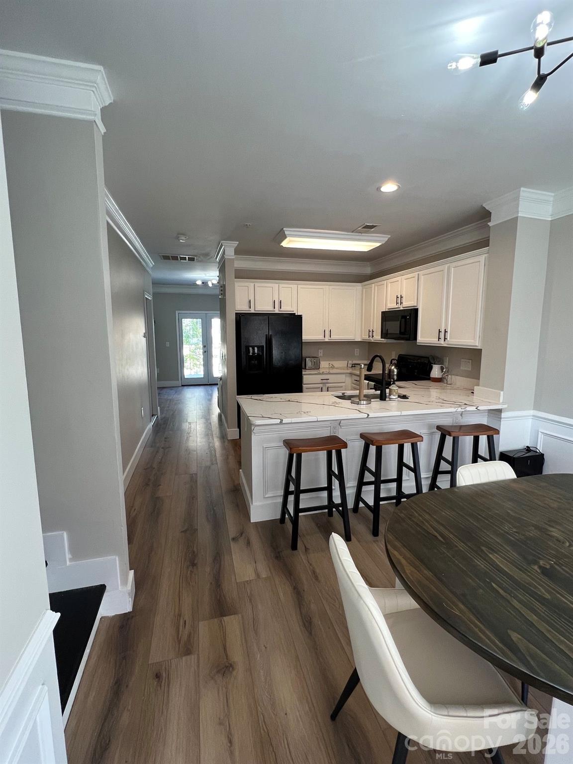 Kitchen with a marble-look island, bar stools, white cabinetry, and wood-look flooring.
