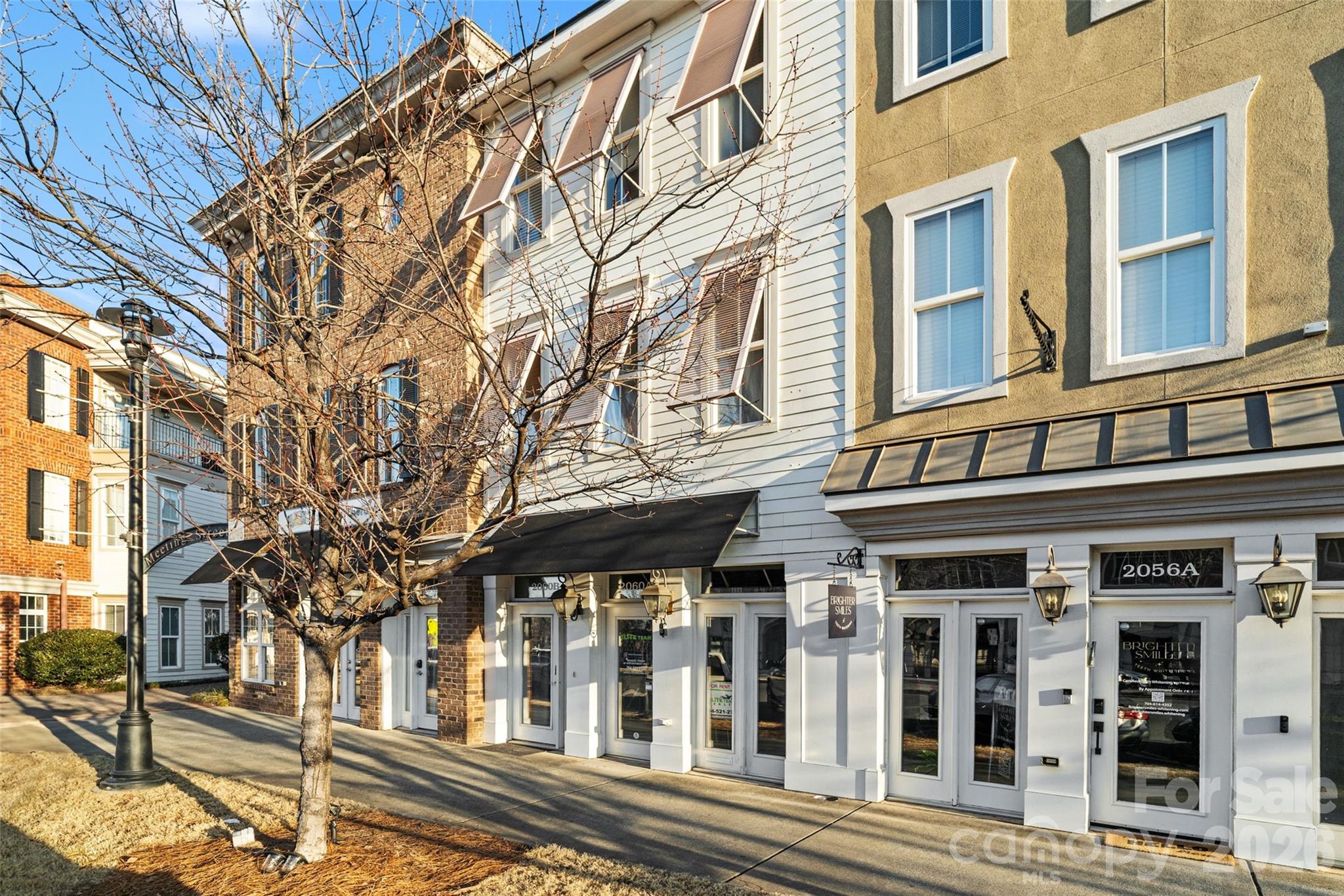 Commercial storefronts beneath multistory facades, with awnings and a leafless street tree.
