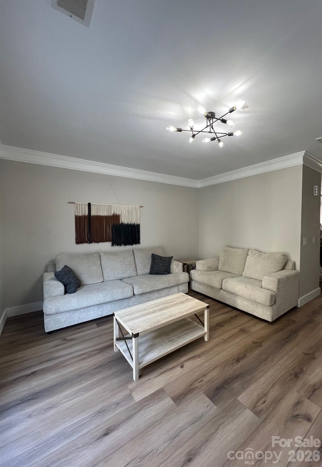 Living room with two light sofas, a pale wood coffee table, and a modern branching ceiling light.