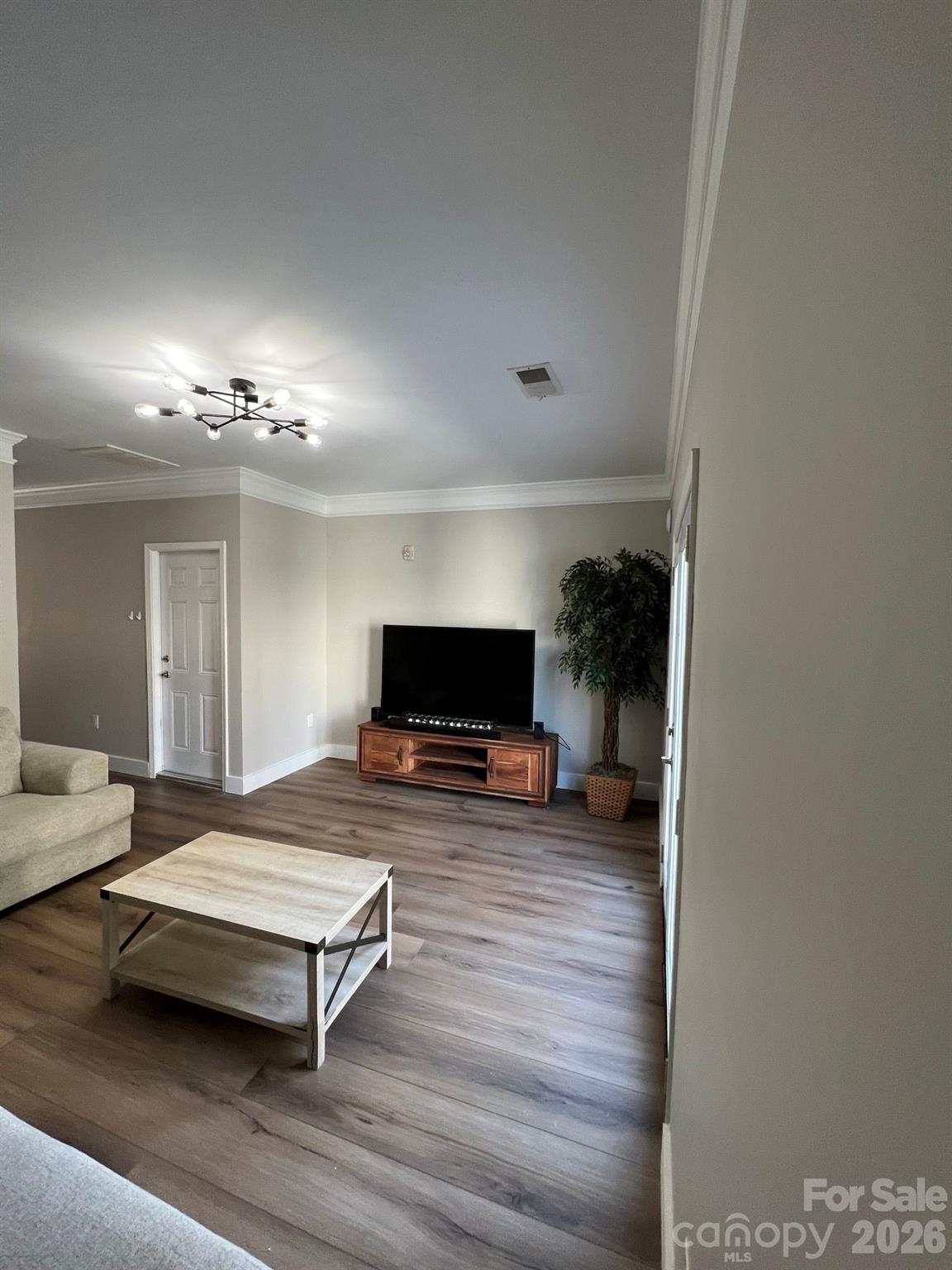 Living room with a television, wooden media console, light coffee table, and wood-look floors.