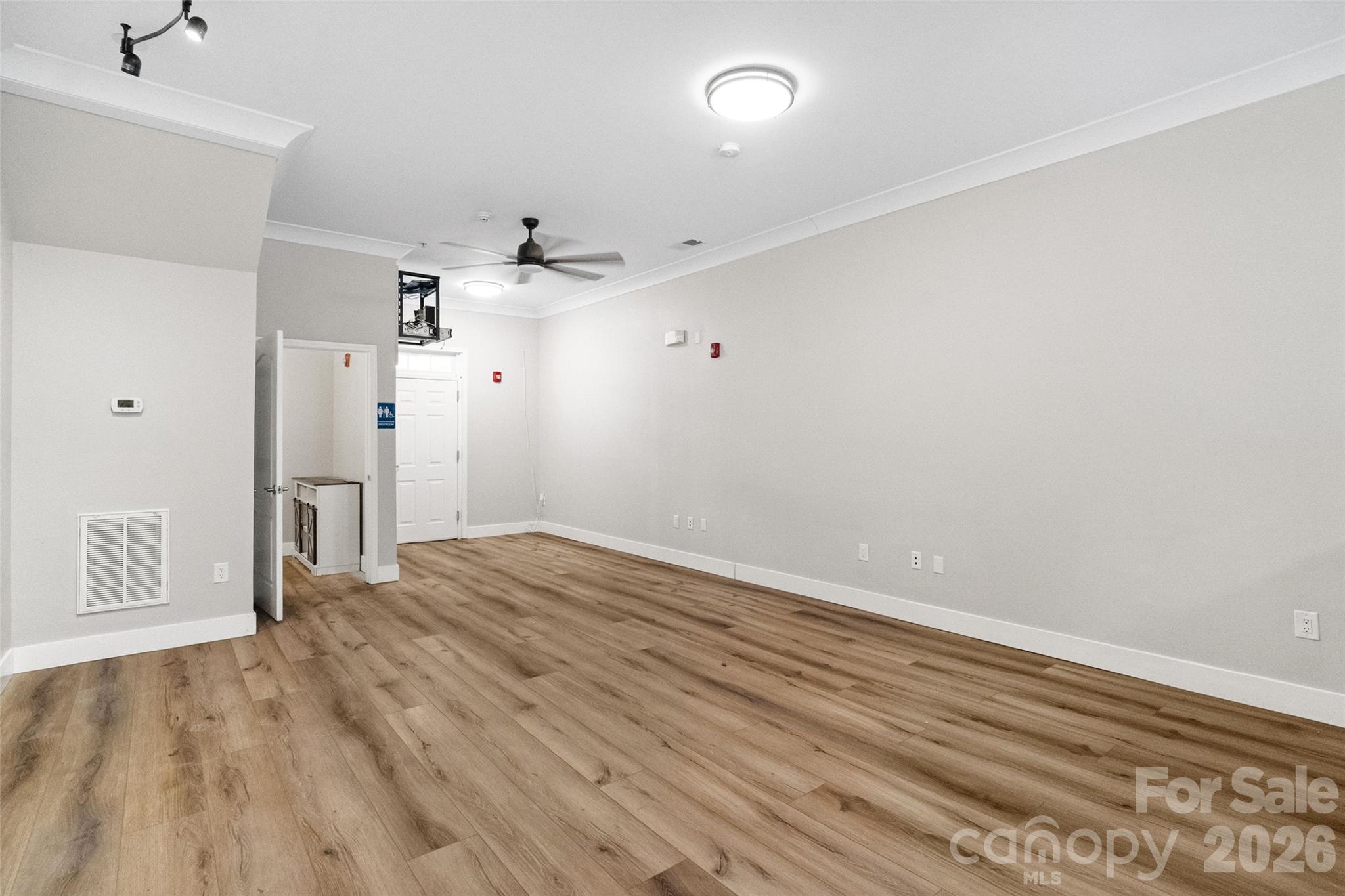 Empty room with wood-look flooring, a ceiling fan, and a doorway at the far end.