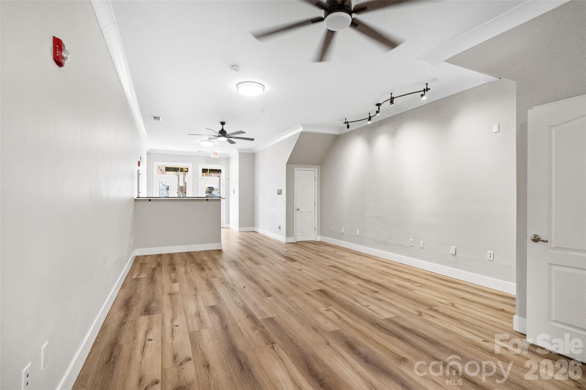 Vacant interior room with wood-look flooring, ceiling fans, and a counter at the far end.