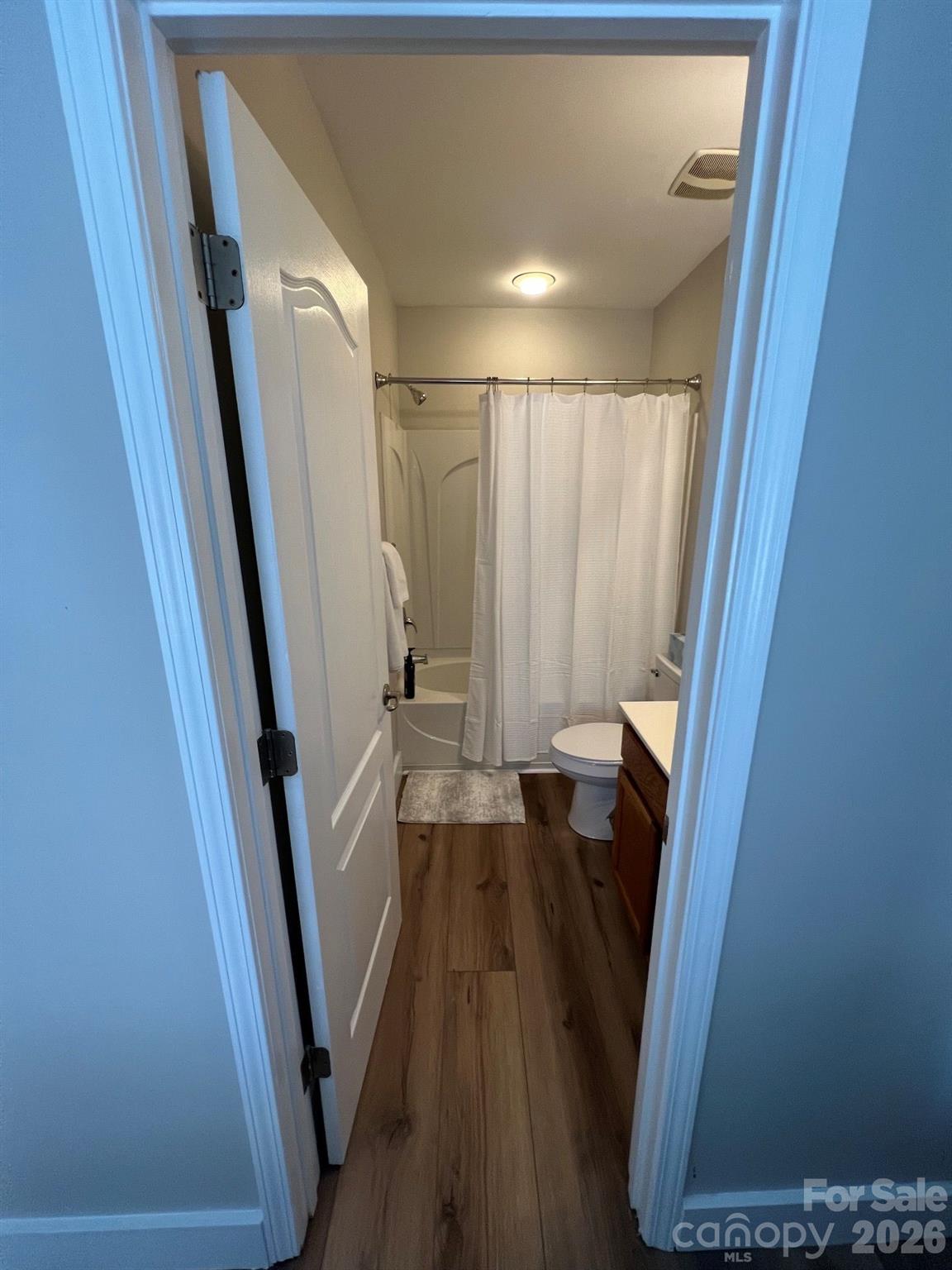 Bathroom with a white shower curtain, toilet, wood vanity, and wood-look flooring.