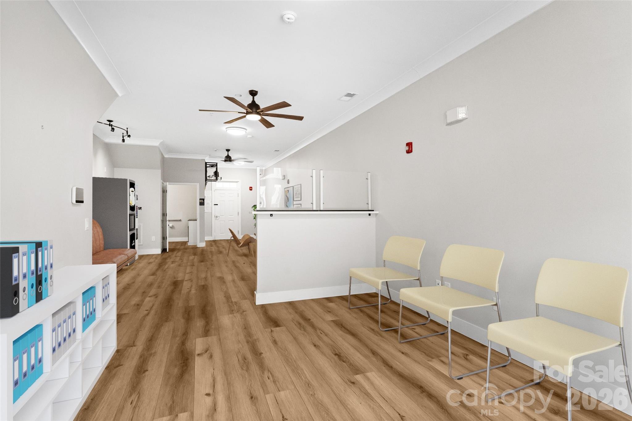 Commercial reception area with a white counter, pale waiting chairs, and wood-look flooring.