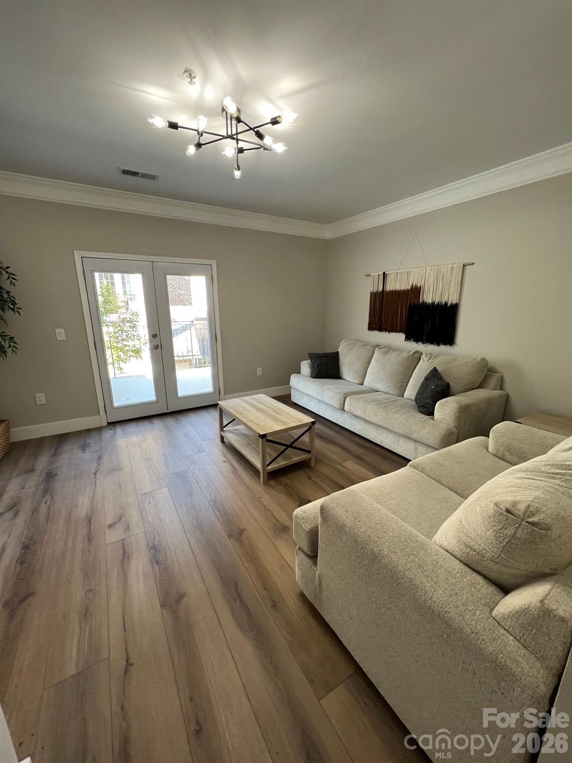 Living room with light sofas, wood-look flooring, a modern chandelier, and glass doors to a balcony.