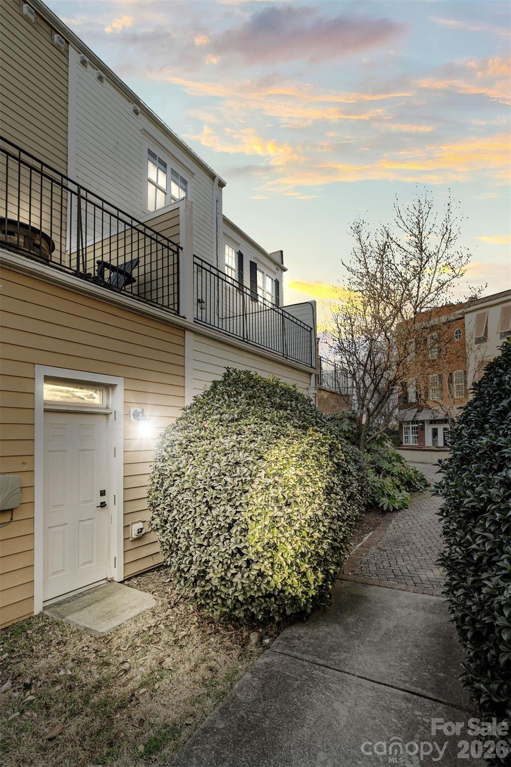 Townhouse exterior with black-railed balconies, a landscaped courtyard, and a brick walkway at sunset.