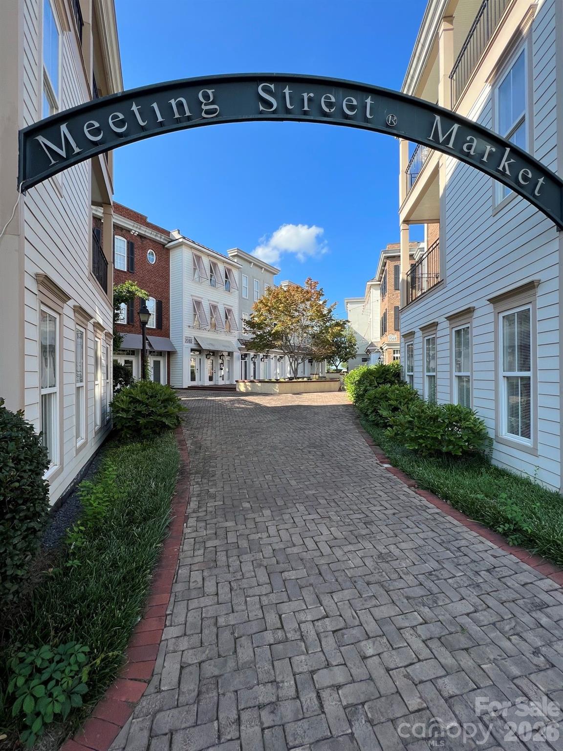Meeting Street Market courtyard with a brick walkway beneath an arched entrance sign.