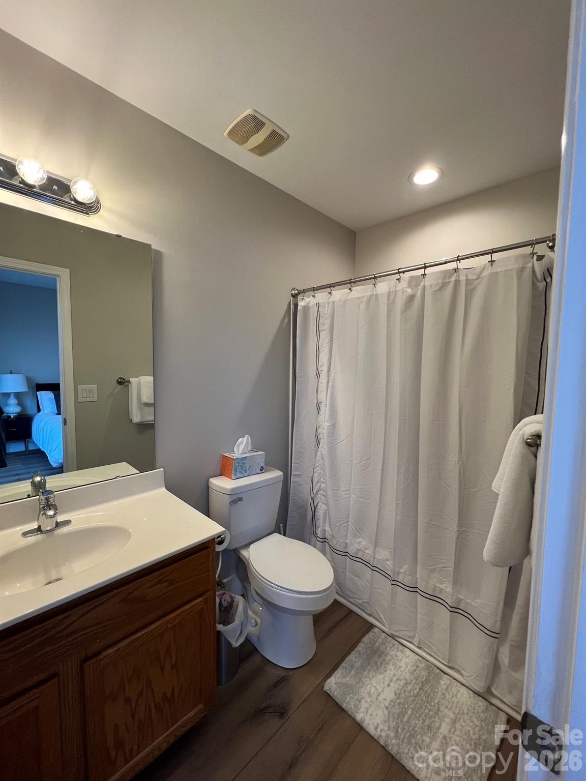 Bathroom with dark wood vanity, white sink and toilet, and a curtained tub-shower.