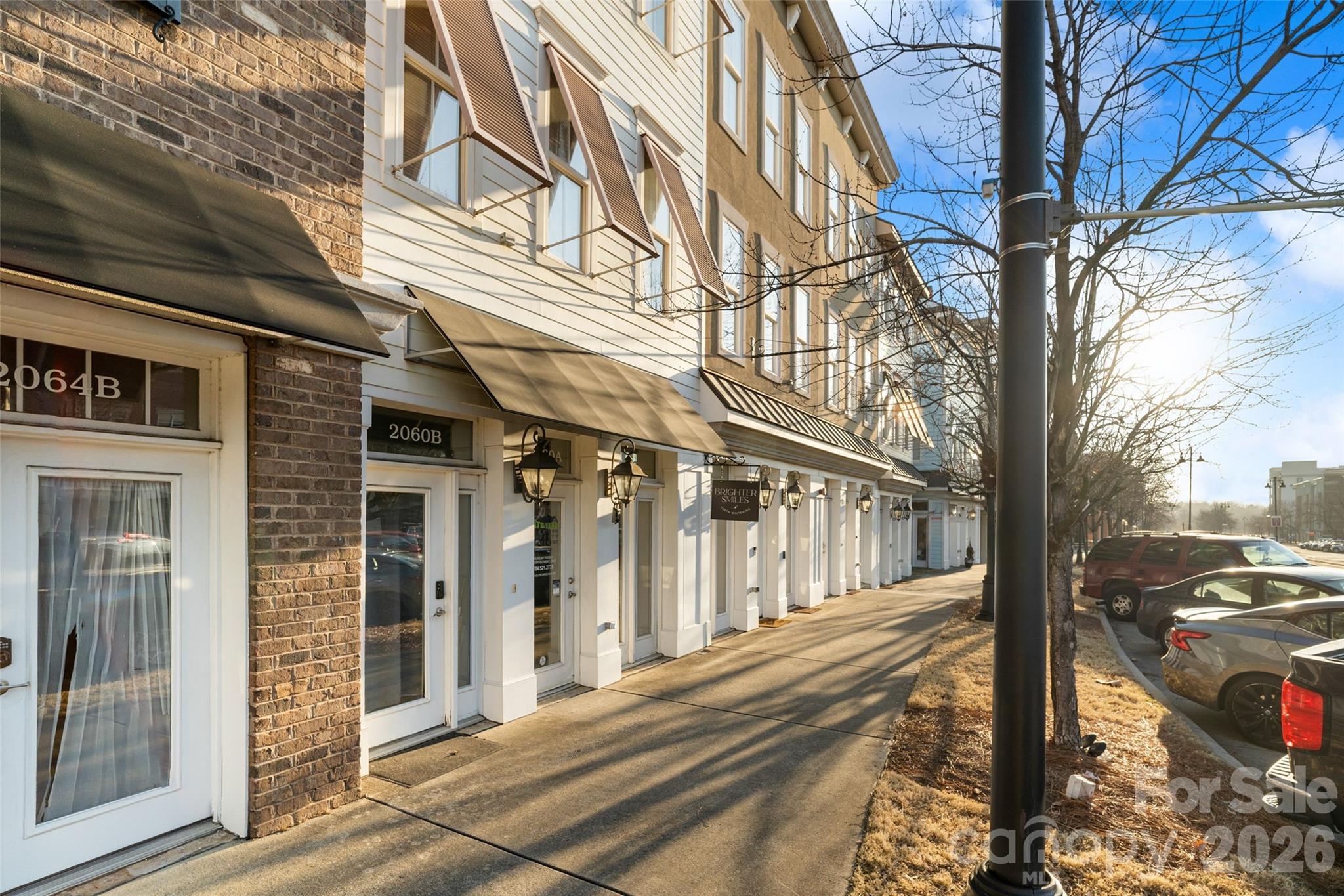 Commercial storefront row with projecting awnings and lanterns along a sunlit sidewalk.