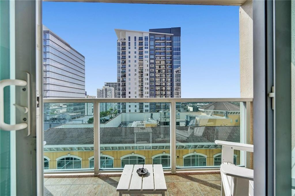 Condominium balcony with glass railing and white patio furniture overlooking downtown high-rises.