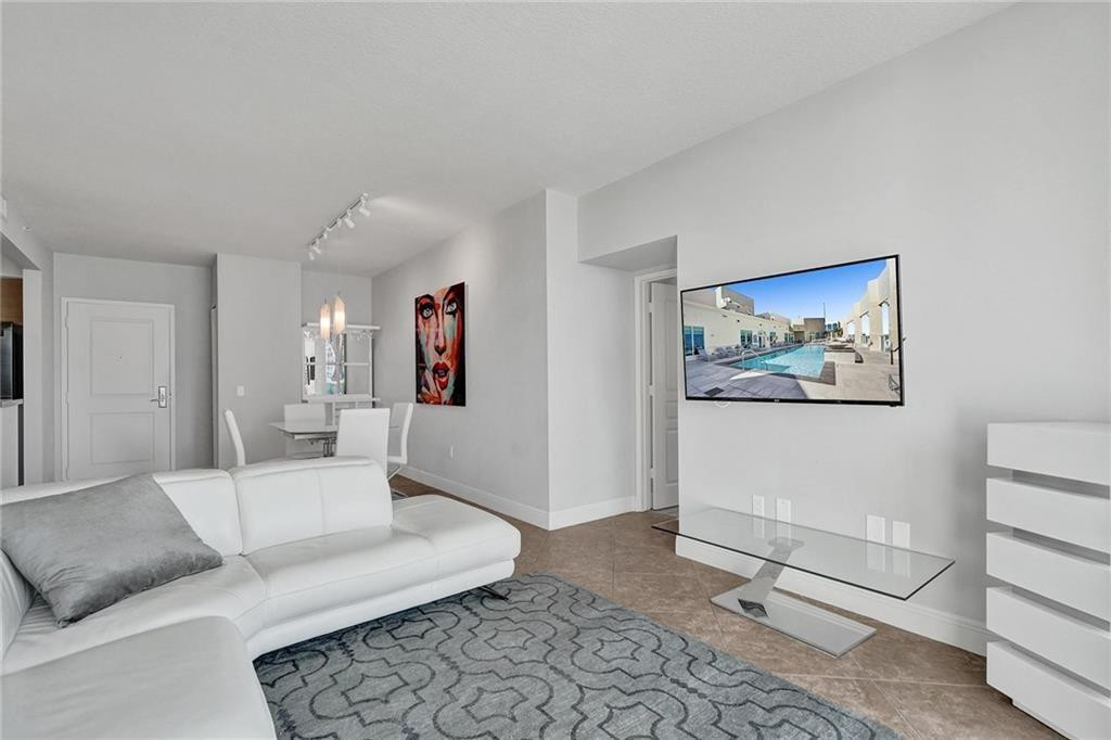 Condo living room with white sectional, gray patterned rug, glass coffee table, and dining area.