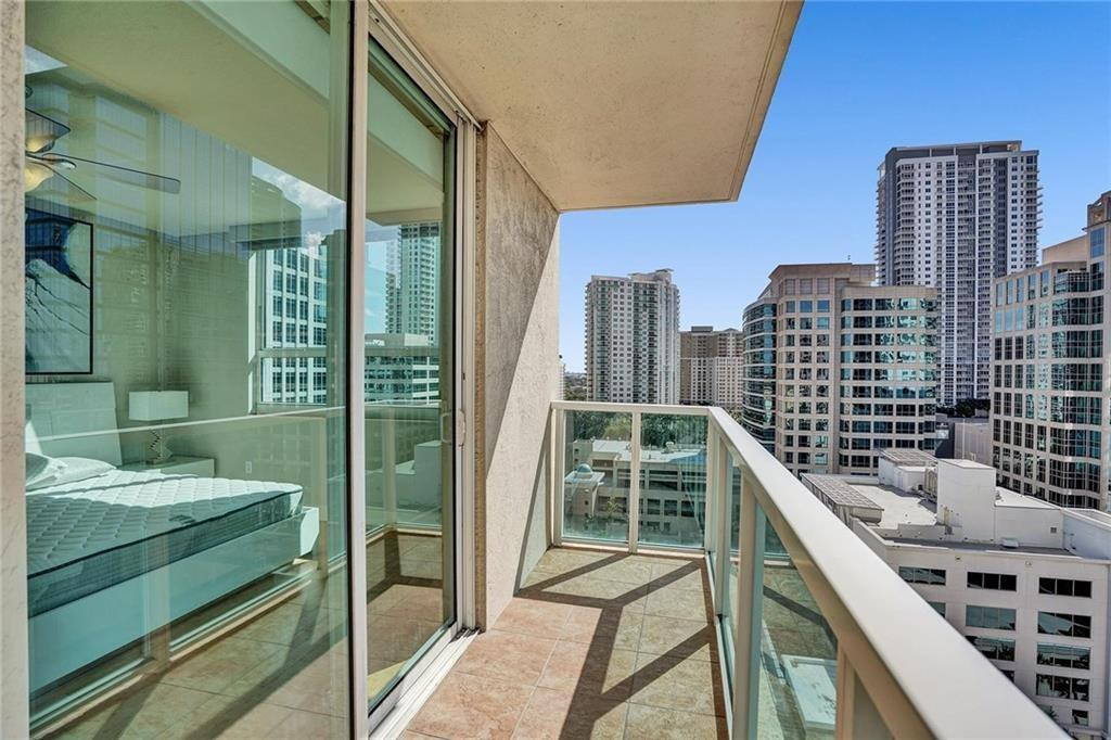 Condo balcony overlooking downtown high-rises, with a bedroom visible through the sliding glass doors.