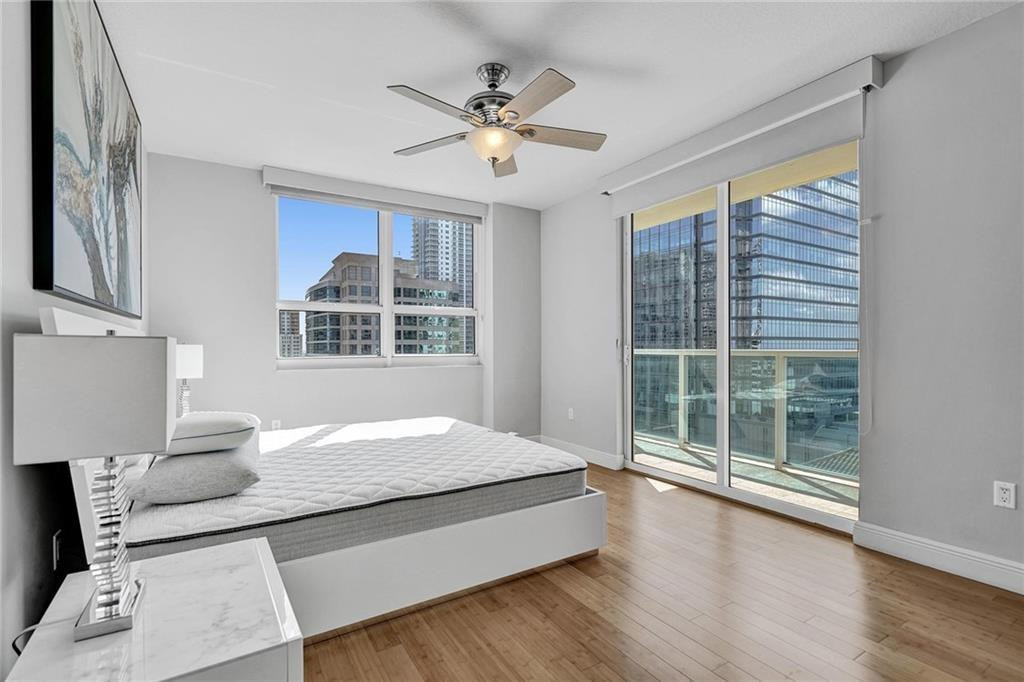 Bedroom with a bed, ceiling fan, and balcony doors overlooking nearby high-rise buildings.