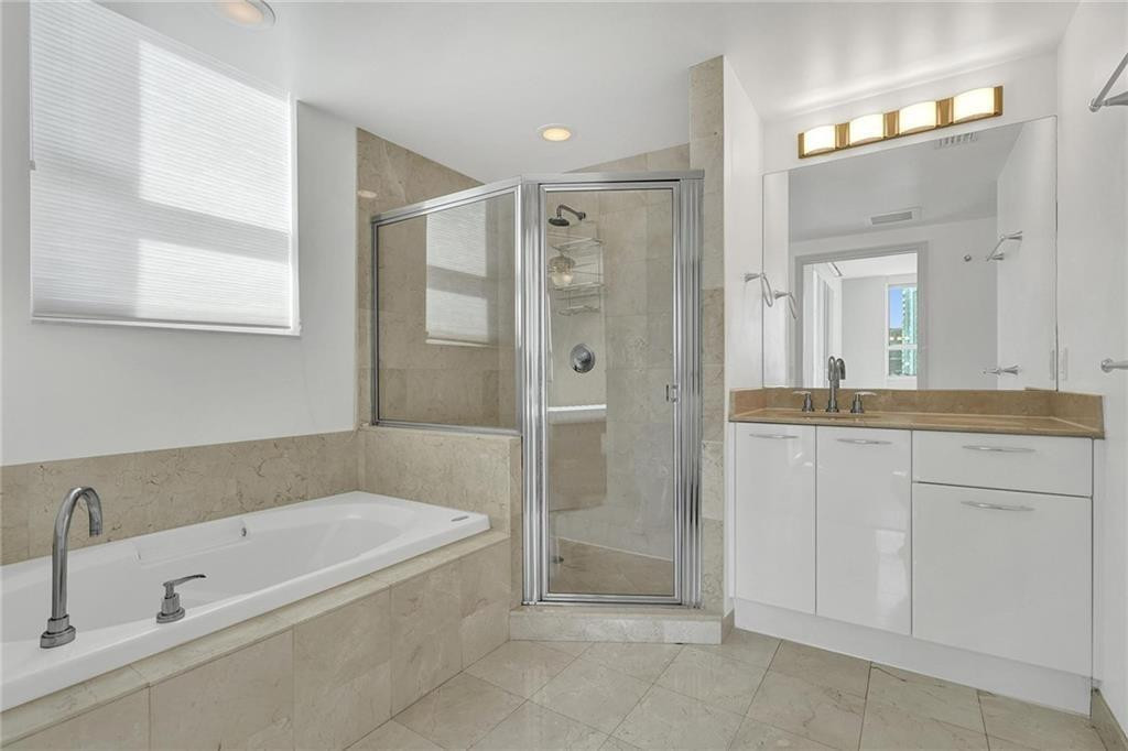 Bathroom with a built-in soaking tub, glass-enclosed shower, and white vanity.