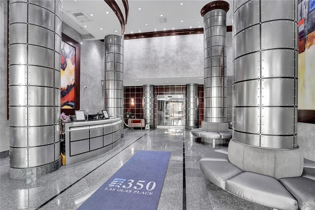 Condominium lobby with a curved reception desk, metallic columns, and gray seating.