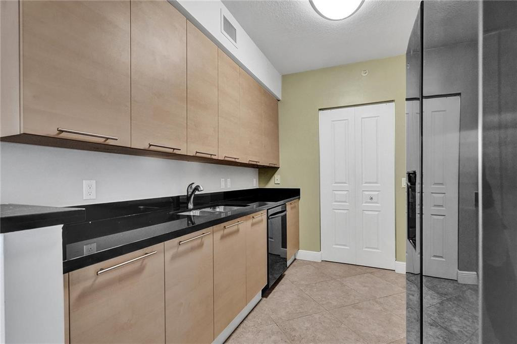 Kitchen with light wood cabinets, black countertops, and a stainless steel refrigerator.