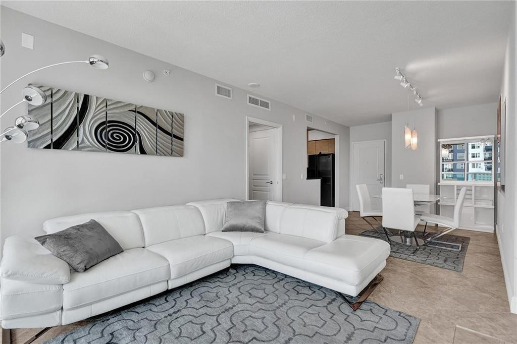 Living room with a white sectional sofa, patterned rugs, and an adjoining dining area.