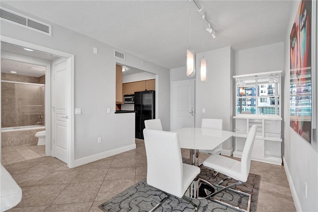 Condominium dining area with a white table, patterned rug, and nearby buildings visible through the window.