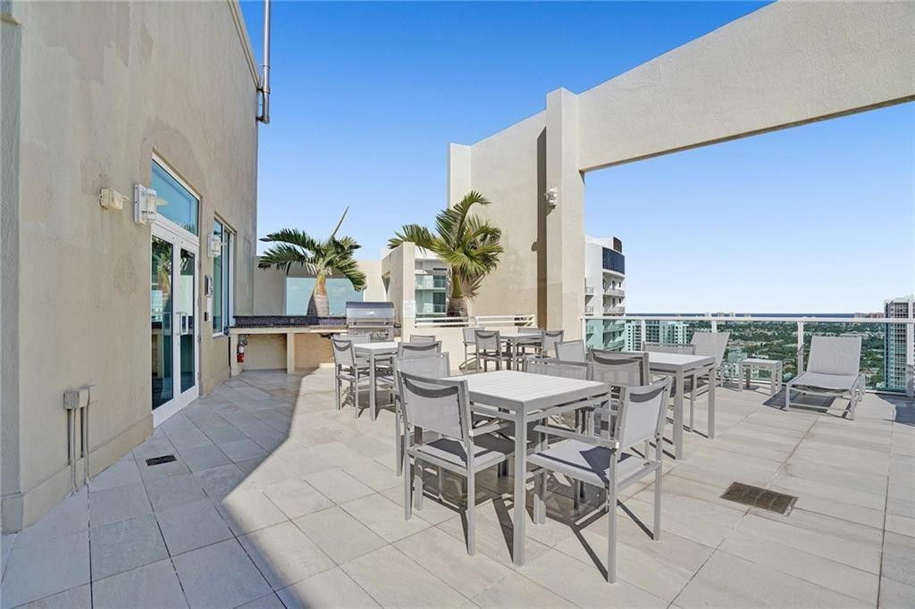 Rooftop terrace with outdoor dining furniture, palm trees, and views of nearby buildings.