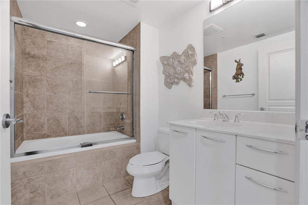 Bathroom with a glass-enclosed tub and shower, beige tile, and a white vanity.