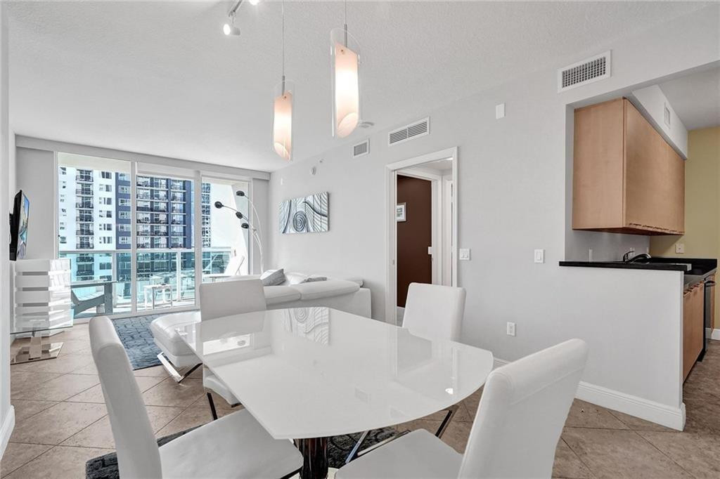Furnished condo living and dining area with a white table, sectional sofa, and high-rise views.